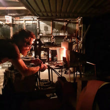 Benjamin working in his old home forge with tools and equipment around, holding a set of long tongs which grip hot steel in the forge.
