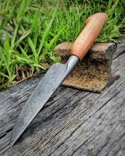 Decorative Damascus knife with a wooden handle on a wooden surface with grass in the background
