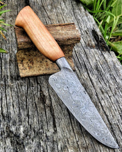 Damascus wrought iron clad knife with a wooden handle on a rustic wooden surface
