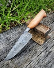 Bridge 189 Chef Knife, Damascus wrought iron blade with a wooden handle on a wooden surface with grass in the background