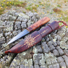Damascus steel Puukko knife with wood handle and embossed gold star compass design on a textured wood surface