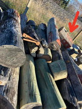 Stack of wooden logs salvaged from Bridge 189 with a red arrow pointing to the actual piece of wood used in the knife handle, outdoors.