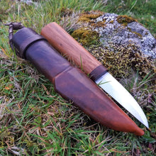 Brown leather sheath and Puukko knife resting on a grassy knoll. 