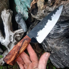 Chefs Knife in the hand of Benjamin, the maker. Behind is a pile of weather worn woods.