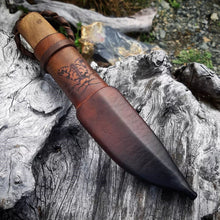 Puukko knife in its leather sheath on a gnarly wood surface