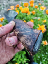 Benjamins hand holding a wooden knife handle with a fossilised whale bone pommel. Blurred orange flowers are in the background