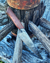 Wagon Wheel Chef Knife with a wooden wagon wheel spoke handle and a shimmering Damascus blade clad in wagon wheel wrought iron, photographed on a Victorian wagon wheel.