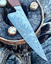 Wagon Wheel Chef Knife with a random patterned Damascus blade clad in wagon wheel wrought iron, photographed on a Victorian wagon wheel.