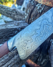 Close-up of a the Wagon Wheel Chef knife highly patterned damascus steel clad in wrought iron on a weathered wagon wheel background.