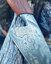 Wagon Wheel Chef Knife detail showing off the patterns of the Damascus steel and wagon wheel wrought iron cladding, photographed against a rugged background 