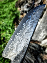 Close-up of a knife blade with a marbled wagon wheel wrought iron pattern against a natural background