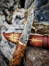 Damascus Puukko knife with redwood handle and gilded compass sheath on a textured background