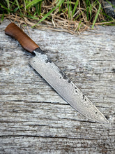 Damascus knife with a Pohutukawa handle on a wooden surface with grass in the background