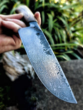 Damascus knife blade with intricate patterns held by Benjamins hand against a natural background