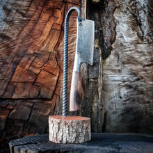 Kitchen cleaver hanging on its custom display stand made from repurposed rebar, with a background of textured wood.