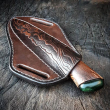 Leather sheathed hunting knife on a textured wooden surface.